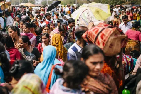 Getty Images Men and women, some with umbrellas to shield from the sun in a crowded Delhi street