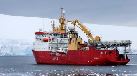 HMS Protector, on an icy ocean with snow covered land in the background