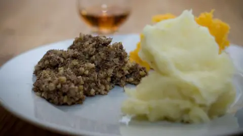 A plate of food with haggis, neeps and tatties being served 