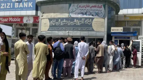 Getty Images Afghan people line up outside AZIZI Bank to take out cash as the Bank suffers amid money crises in Kabul