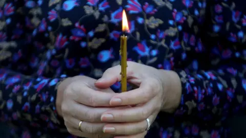 Getty Images A woman holds a candle at a memorial in Ukraine
