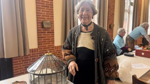 A woman with grey hair stood next to her glass terrarium which has been repaired.