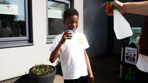 Reuters A pupil is sprayed with a fine mist as they drink water at the Harris Academy Primary Maxyflower school, as Britain experiences record temperatures disrupting schools and transport networks, in Grays, Britain, June 24, 2026. 