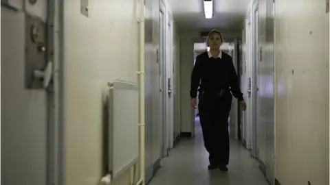 Getty Images A female prison officer walks down the corridor of a prison's residential wing