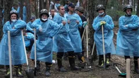 Reuters Emergency workers wearing blue plastic coverings as they dig