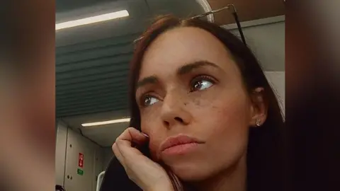A photograph issued by police of Jade Downes. She has brown eyes and long brown hair and is resting her face in her hand, looking thoughtful.