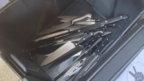 A black bin/box with multiple knives that people have surrendered on 29 September 2024