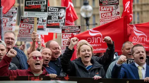 Getty Images A group of men and woman, some holding red flags and other holding black placards, some of which read: "Save Lindsey Oil Refinery".