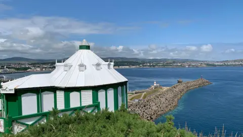 BBC The exterior of the Camera Obscura, a domed white and green son Douglas Head, with Douglas Bay in the background on a sunny day.