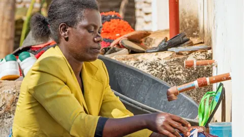 Suzanna Kathumba, in a yellow jacket, washes clothes at an outside tap in Lilongwe, Malawi.