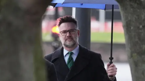 An image of TV auctioneer Charles Hanson wearing a black coat whilst holding an umbrella