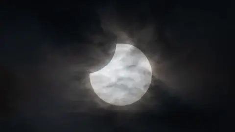 A partial solar eclipse, the sky is black and the moon in the middle. 