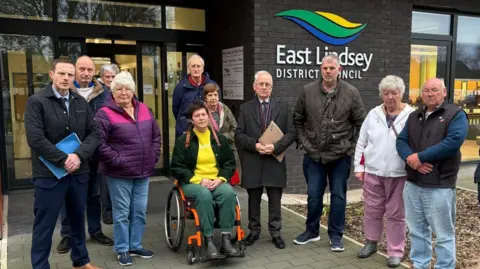 Members of the Save Wood Lane group standing outside the East Lindsey District Council building. They are dressed in warm clothing and are looking at the camera. 