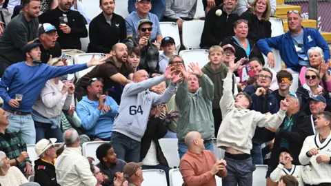Getty Images A group of spectators at a cricket match try to catch a ball which is flying into the crowd.