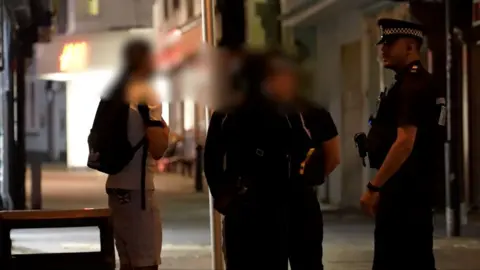 Jamie Niblock/BBC Teenagers with blurred out faces talking to police officers in a street in Ipswich at night