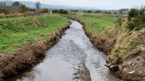 Loughs Agency Shows a river with banks on either side and mountains in the background