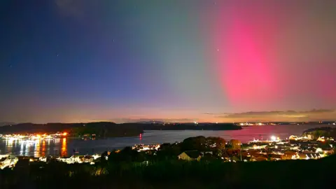 Cara/BBC News NI Weather Watcher A landscape photo taken at night from a hilled area showing the Northern Lights in the sky. There are streaks of green, blue and pink lights.