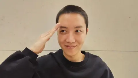 J-Hope via Weverse J-Hope with a buzzcut saluting.