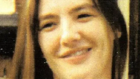 A printed photograph of Gemma Simpson. She is smiling, looking off camera. She had straight brown hair.