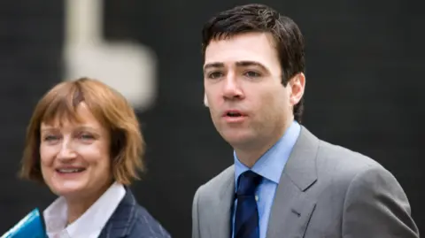 Getty Tessa Jowell (left) has chin-length light brown hair and wears a white shirt and navy checked suit jack. Andy Burnham (right) has dark short hair and wears a grey suit with a blue shirt and navy-blue striped tie.
