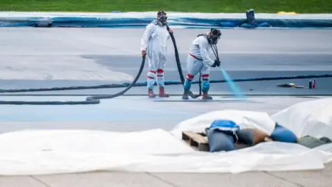 Reuters Workers in paint suits and gas masks spray-painting the pool surface blue