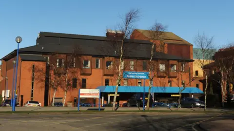 A general view of Scarborough Hospital, a red‑brick hospital building with a blue canopy.