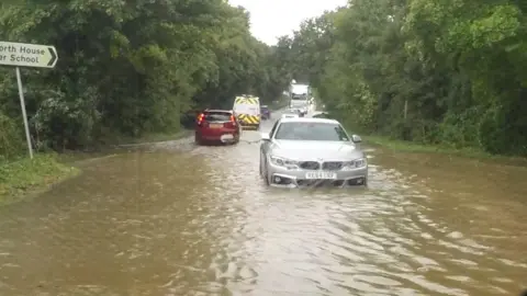 A car driving through deep muddy water, which is almost up to its number plate