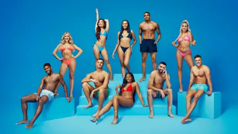 ITV/Shutterstock André Furtado, Molly Marsh, George Fensom, Ruchee Gurung, Ella Thomas, Catherine Agbaje, Tyrique Hyde, Mehdi Edno, Jess Harding and Mitchel Taylor all in swimwear, posing in front of a blue background