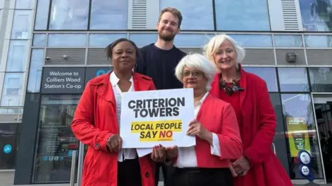 Colliers Wood's Labour Councillors and Mitcham and Morden MP Dame Siobhain McDonagh (right) outside Britannia Point. Three wear road coats and one man wears black. The sign says "Criterion Towers Local People Say No".