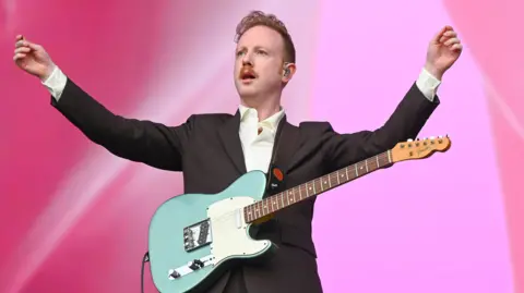 Alex Trimble from Two Door Cinema Club is on stage with his guitar, his arms aloft.