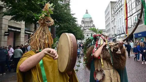 People in mumming outfits with Belfast city hall in background