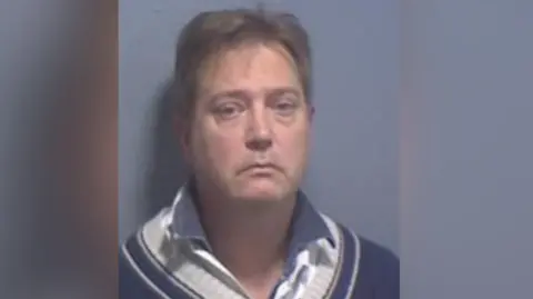 A mugshot of Gregory Manson, who has been jailed at Canterbury Crown Court. Gregory is wearing a navy jumper and shirt underneath.