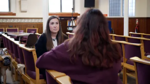 BBC / JOSIE HANNETT 'Jane' sat with her back to the camera in front of reporter Josie Hannett, sat in a church