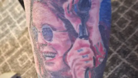 Simon Humphreys Tattoo of Ozzy Osbourne which is him smiling at a microphone stand with round sunglasses on. 