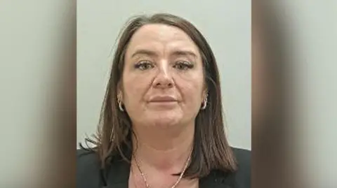 Custody image of Donna Pope. She has shoulder length brown hair and gold earrings and necklace and wears a black jacket.