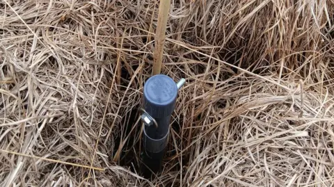 Moors for the Future A metal and plastic device sticking out of dry grass.