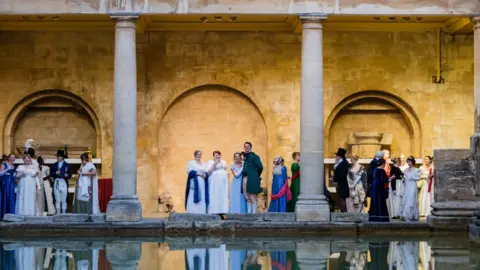 Jane Austen Festival People in regency era clothing are standing by the Roman baths in Bath. 
