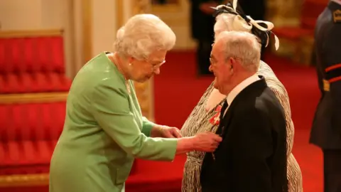 Lewis Whyld Ronald Jones and Penelope Jones receiving their MBE from Queen Elizabeth II