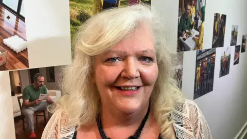 Deirdre has long blonde curly hair and is standing in front of the AI-generated images.