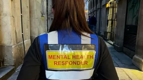 Hope Against Suicide The back of a mental health responder. They are wearing a blue vest with the words 'mental health responder' written in red on a yellow background.