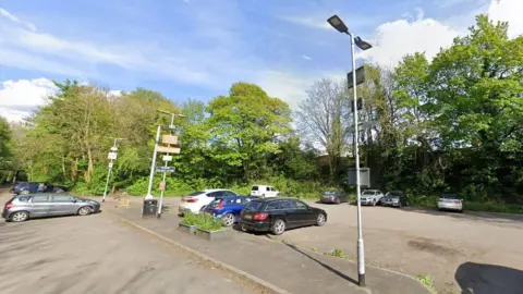 Google car park in Wetherby showing about 10 cars parked, with trees and spotlights 