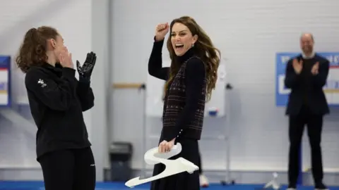 PA Media The princess is cheering with a huge smile on her face on the curling rink while a member of staff stands next to her, clapping her hands and laughing.