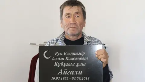 Azh.kz Esengali Supygaliev holds the headstone of his brother Aigali, Kazakhstan, 2018