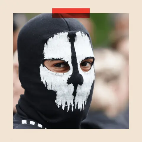 PA A figure wearing a mask at an anti-immigration protest outside Waltham Forest Immigration Bureau in Walthamstow, London