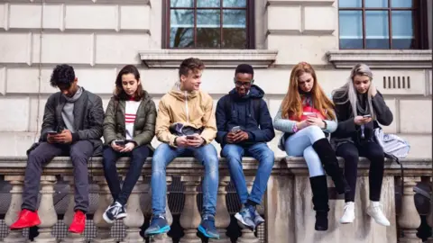 Group of young teenage students or pupils using mobile phones on a school break.