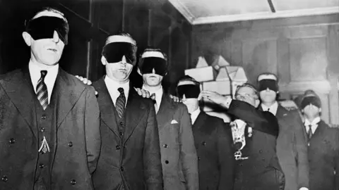 Gamma-Keystone via Getty Images A black and white photo shows a group of men being led wearing blindfolds through a room during an initiation ceremony at a Freemasonry Lodge in 1933.