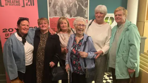 Six women in a row in a theatre.