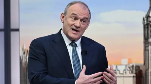 Sir Ed Davey sat in a navy suit with a blue patterned tie, in conversation during the Sunday with Laura Kuenssberg panel show