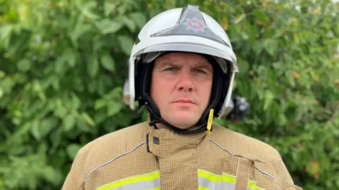Head and shoulders shot of Warren Hathaway looking serious, wearing fire uniform with a white helmet.