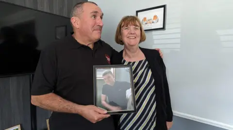 Arline and David Hursey smile proudly while holding a framed photo of their son James.